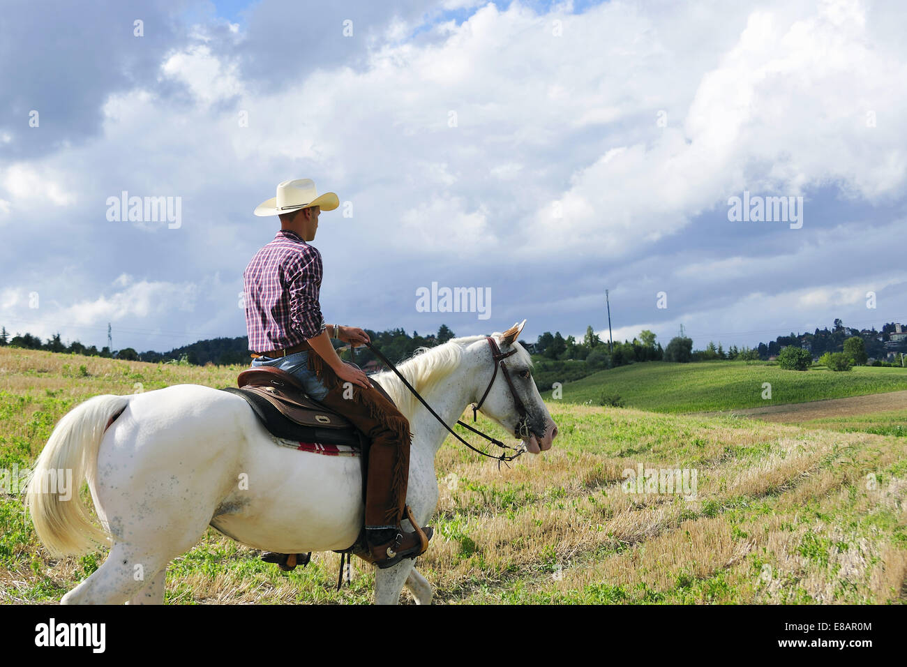 Young man in cowboy gear horse riding in field Stock Photo