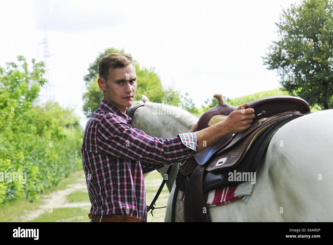 Portrait of young man saddling horse Stock Photo