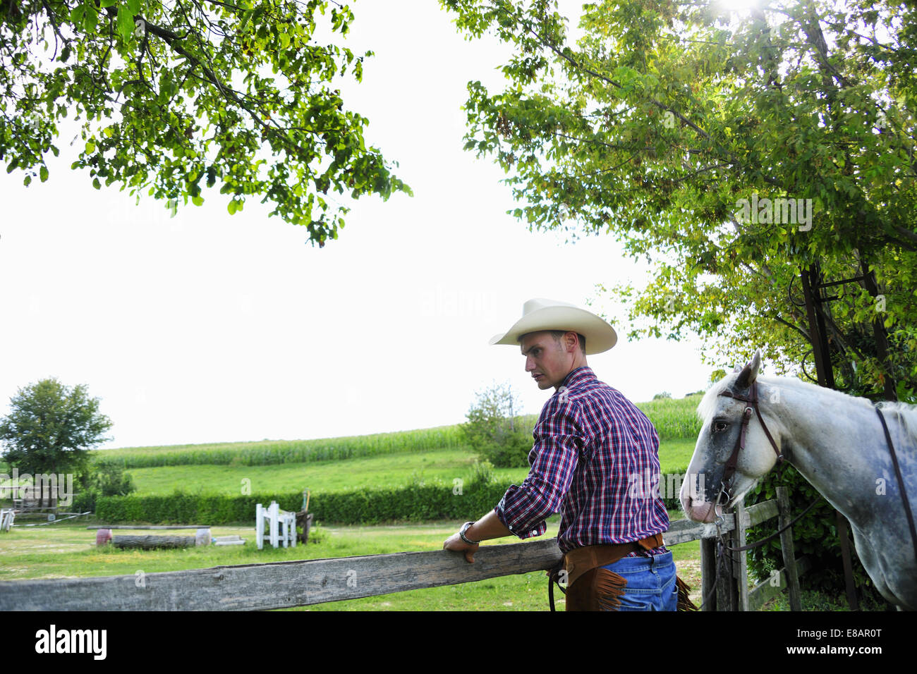 Young man in cowboy gear with horse checking fence Stock Photo