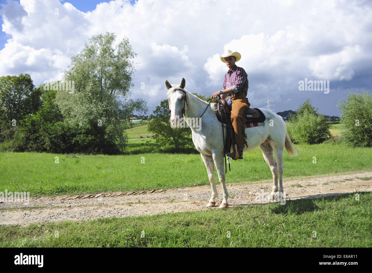 Portrait of young man in cowboy gear on horseback on dirt track Stock Photo
