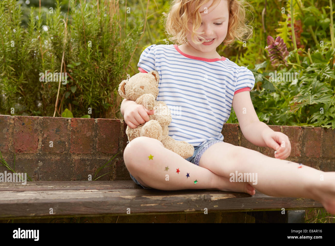 Girl sticking stars on legs on garden seat Stock Photo