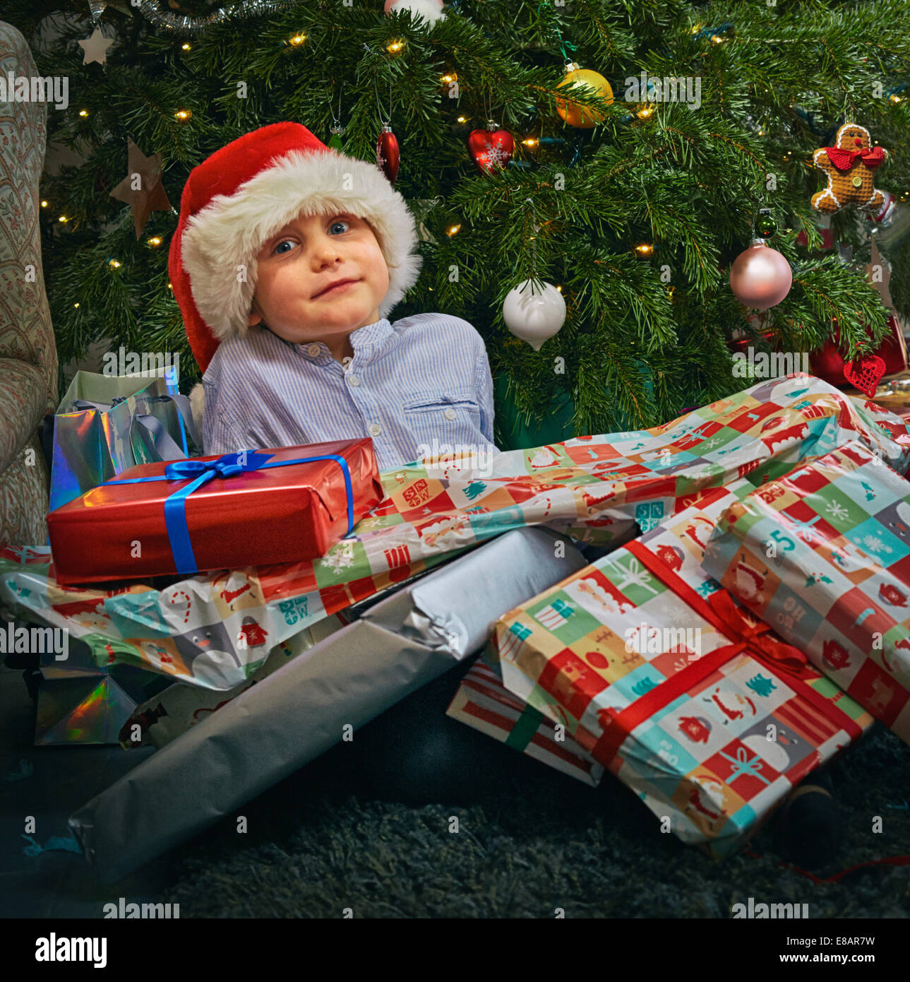 Portrait of cute boy sitting on floor with christmas presents on top of him Stock Photo
