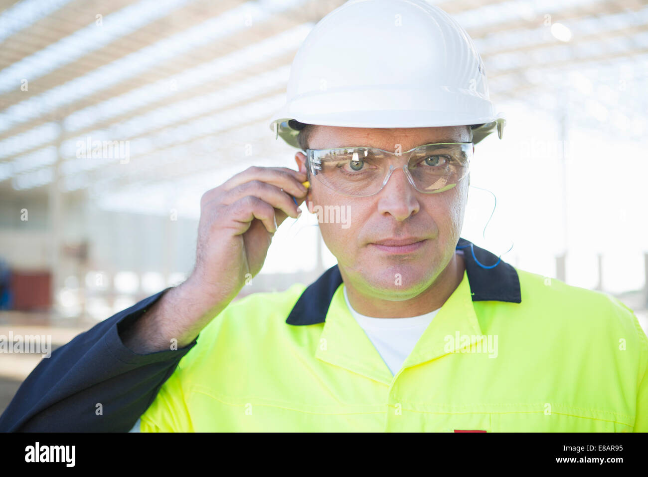 Builder with safety glasses inserting earplugs on construction site