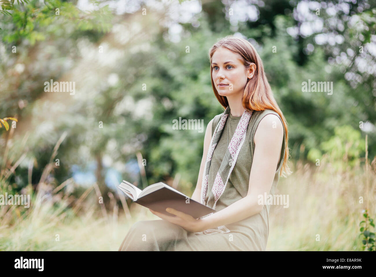 Young woman in field distracted from reading book Stock Photo