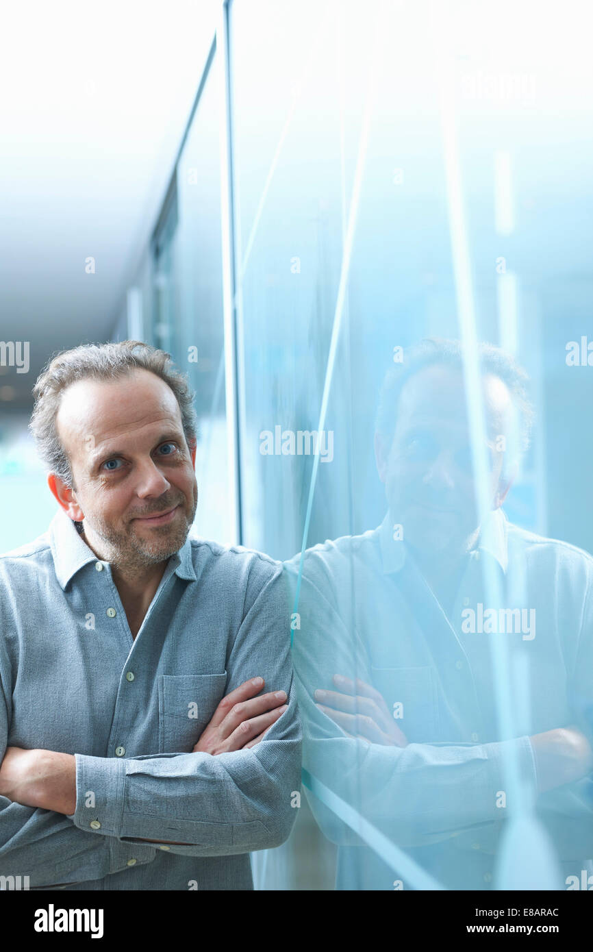 Confident mature businessman leaning against glass wall in office Stock Photo