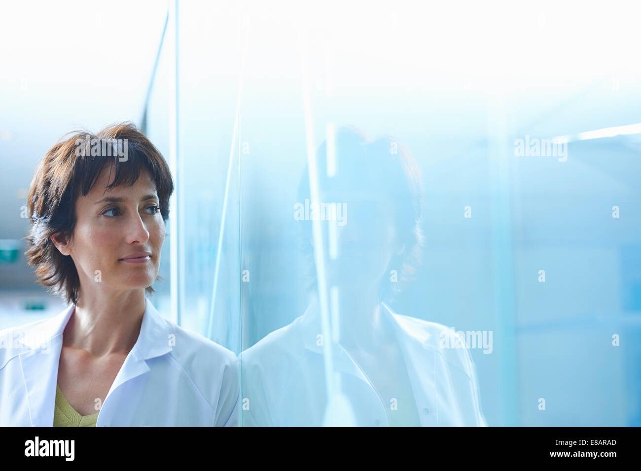 Confident mature businesswoman leaning against glass wall in office Stock Photo