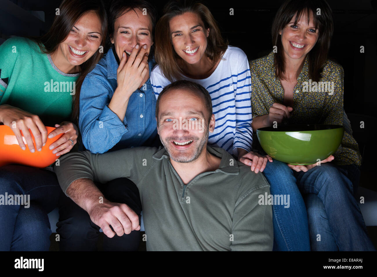 Five adult friends laughing and watching TV with snack bowls Stock Photo