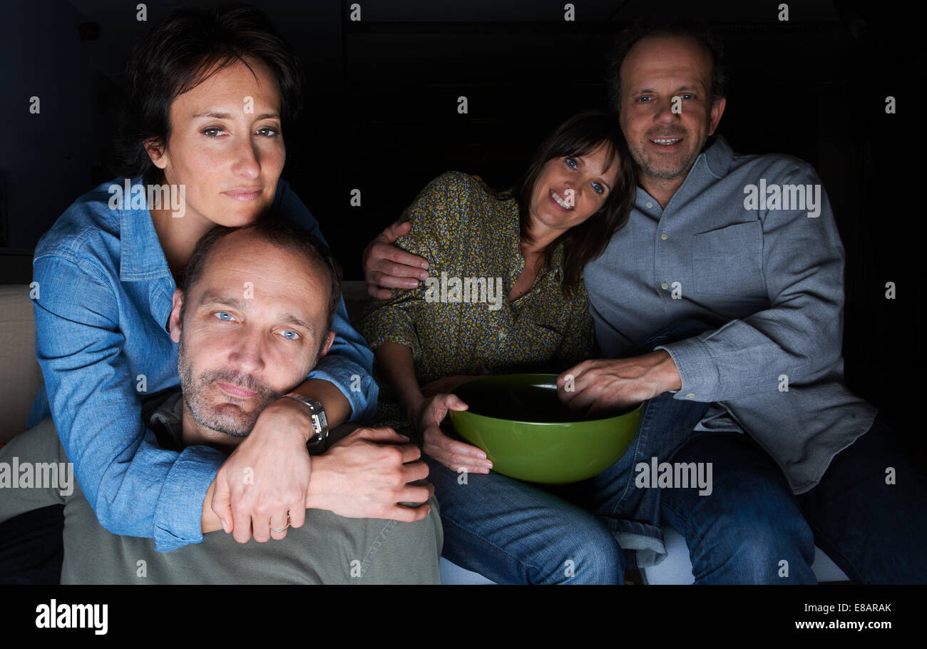 Two mature couples watching TV with snack bowls Stock Photo