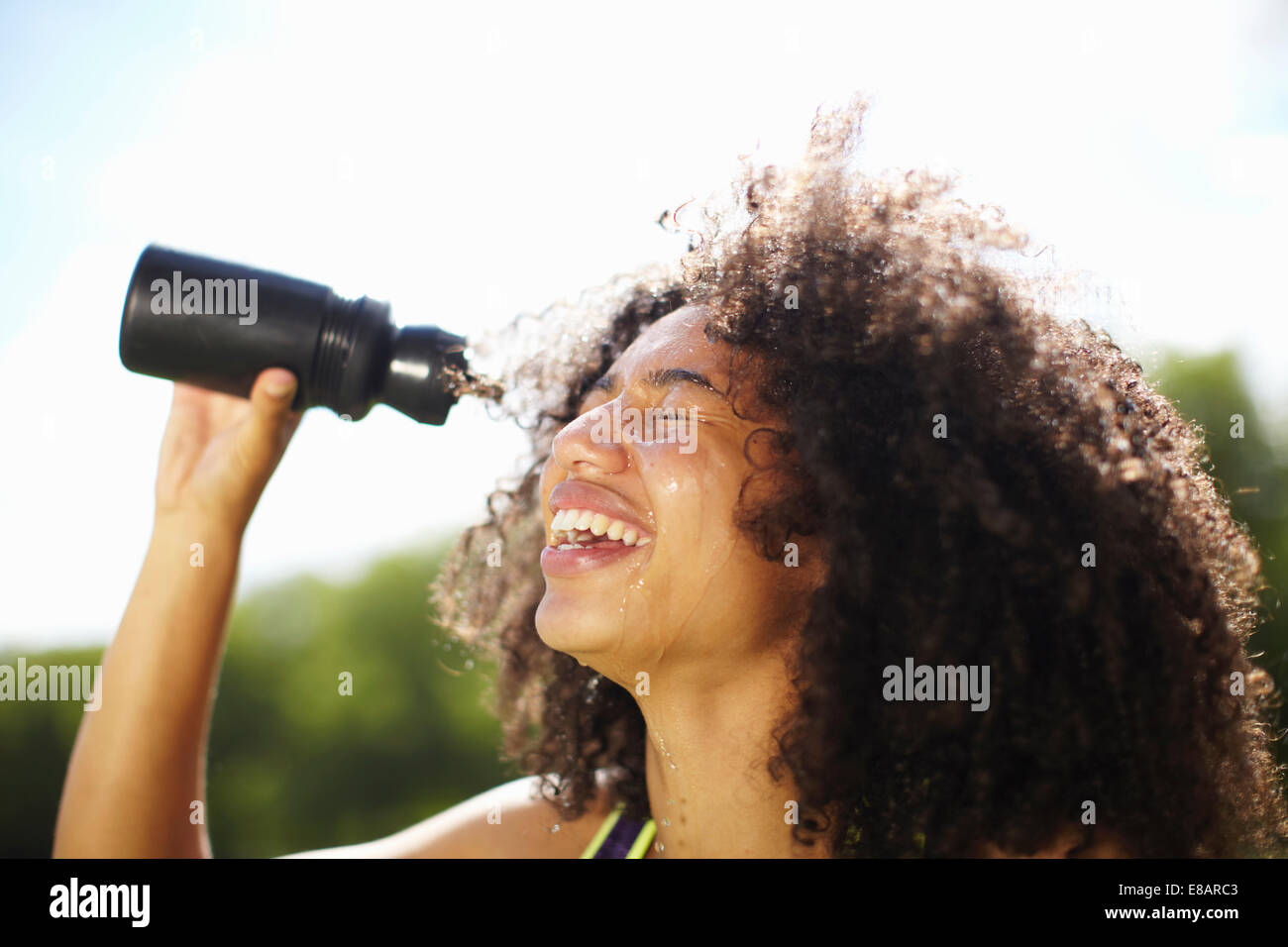 Young woman pouring water onto face in park Stock Photo