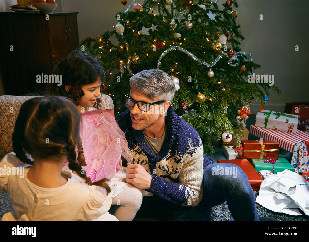 Father and two daughters opening christmas gifts in sitting room Stock Photo