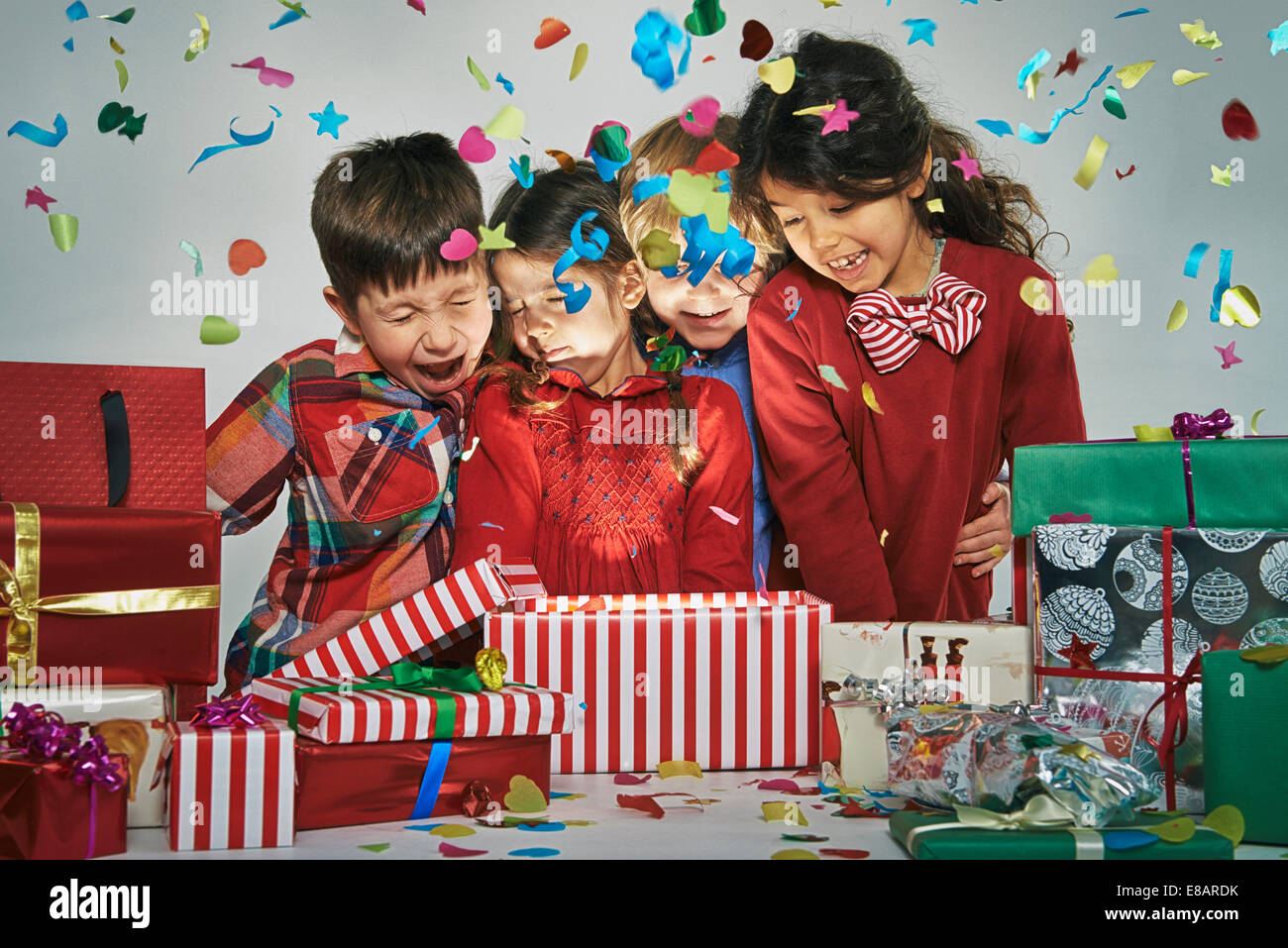 Surprised brothers and sisters unwrapping glowing christmas gift box with exploding confetti Stock Photo