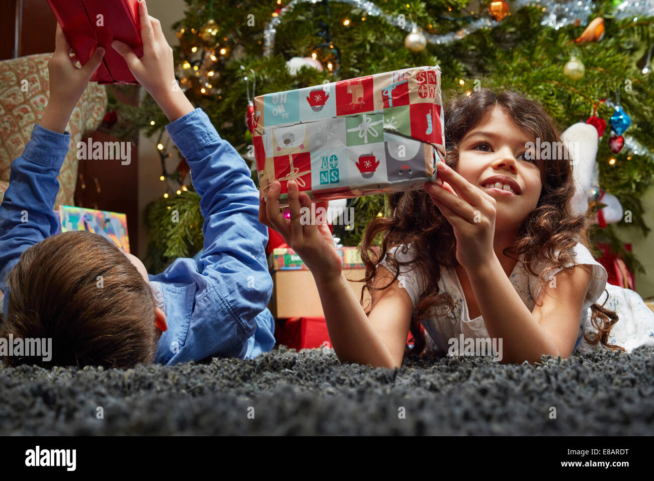 Sister and brother lying in sitting room holding up christmas gifts Stock Photo