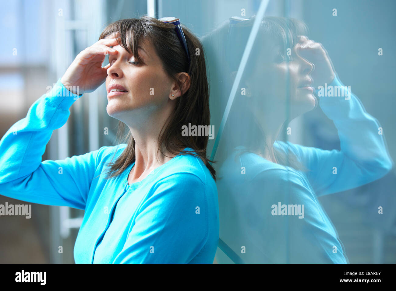 Mature businesswoman leaning against glass wall in office with hand on face Stock Photo