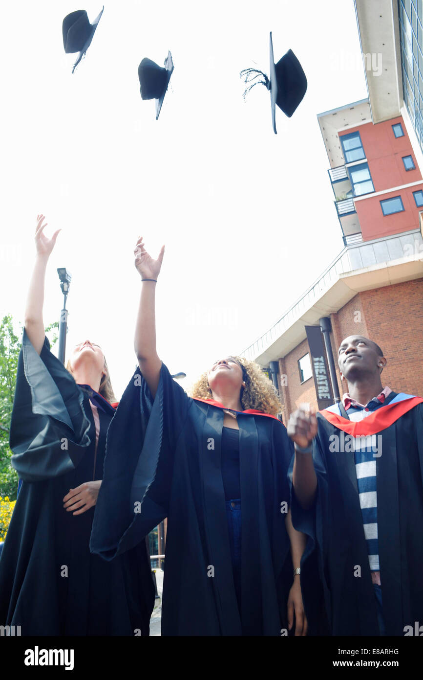Three college students throwing graduation caps mid air Stock Photo