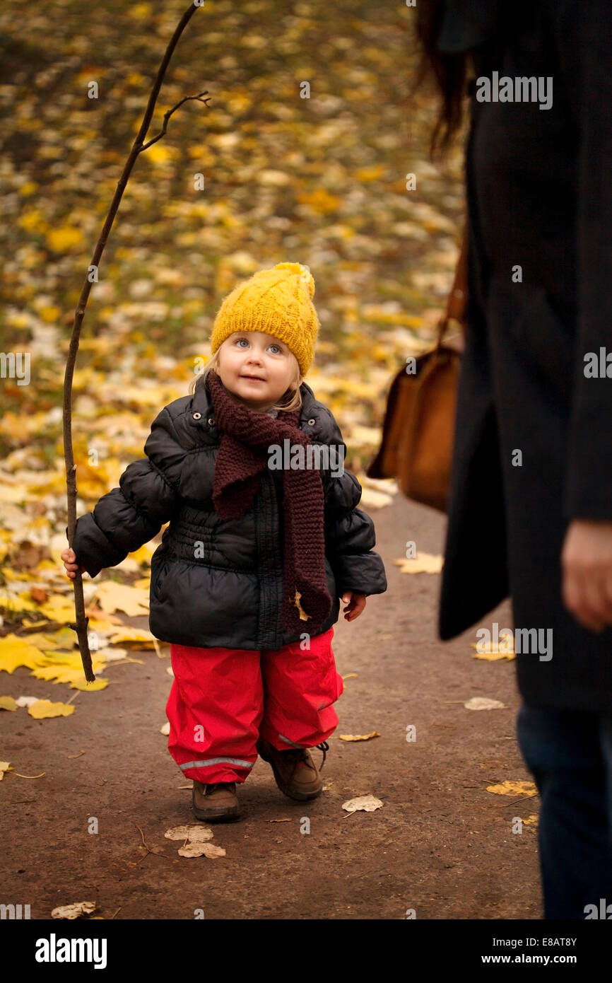 Young girl on walk wearing winter clothes, holding stick Stock Photo