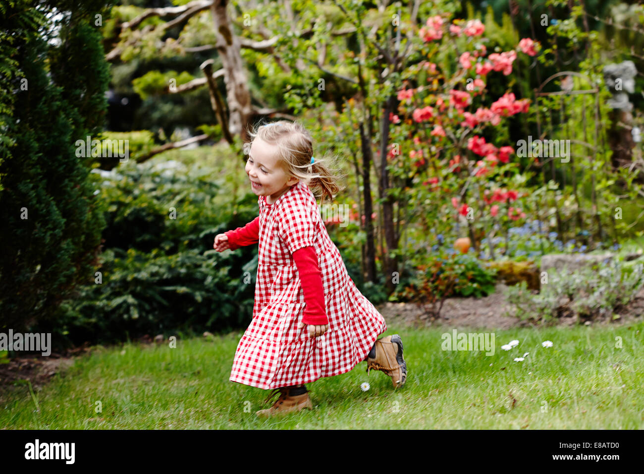 Young girl wearing gingham dress running in garden Stock Photo