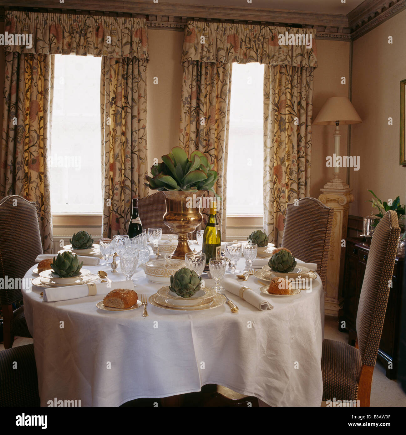 Dining room with green leaves in gold vase on table set for lunch with fresh artichokes on gilt crockery Stock Photo