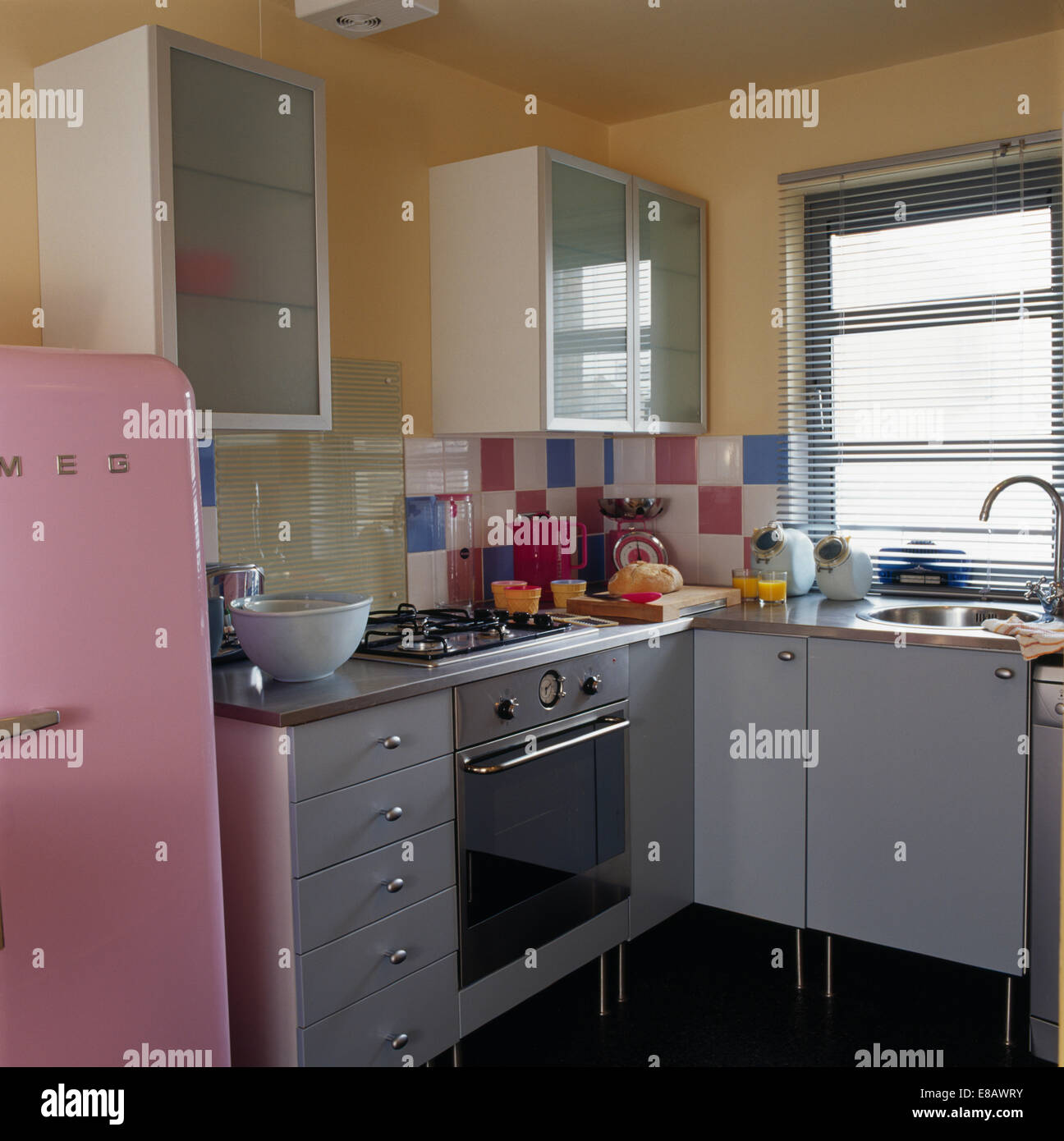 Stainless-steel oven in small retro-style kitchen with Venetian blind on window above sink Stock Photo