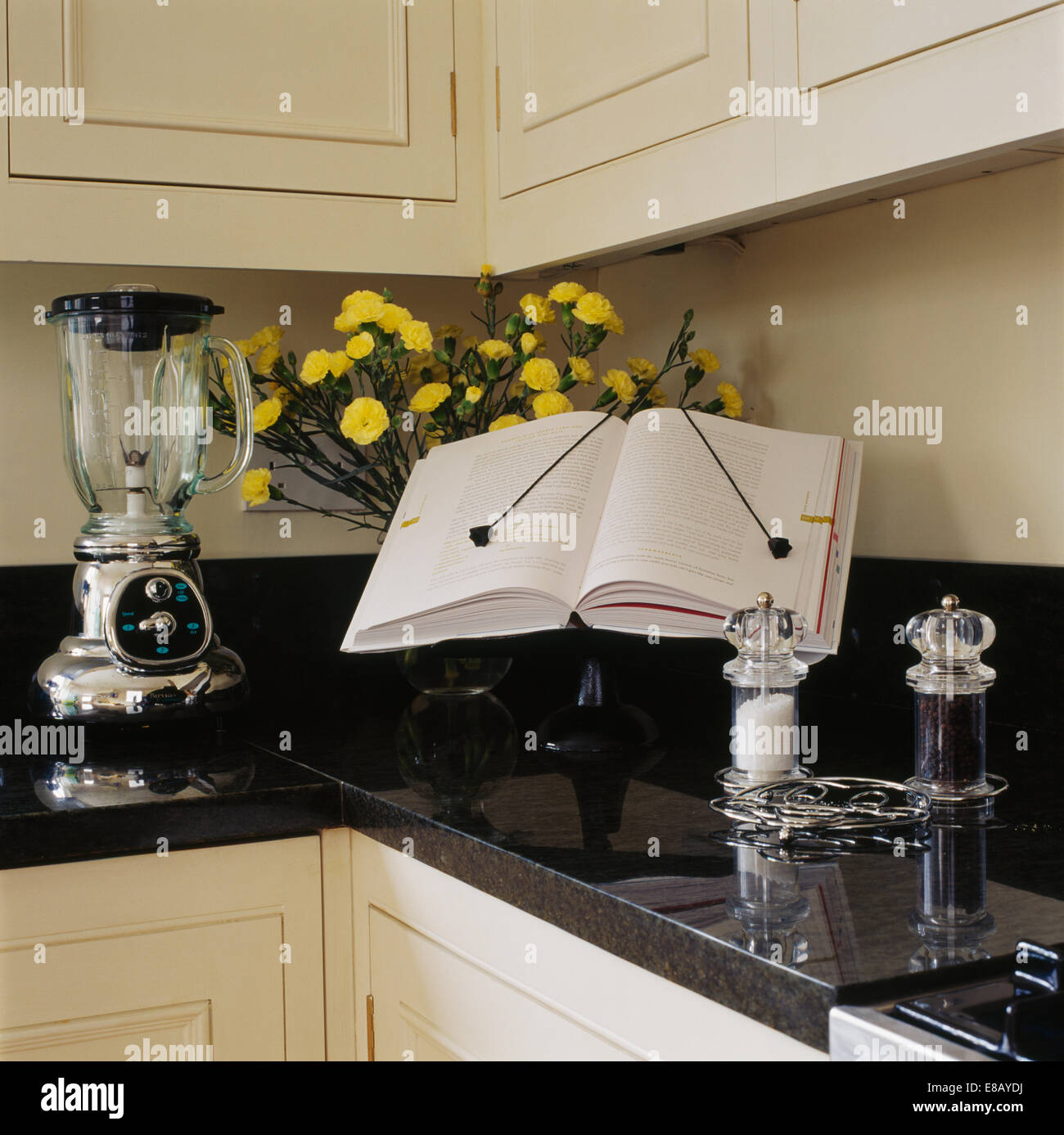 Close-up of cookery book propped open on stand beside electric blender on black granite kitchen worktop Stock Photo