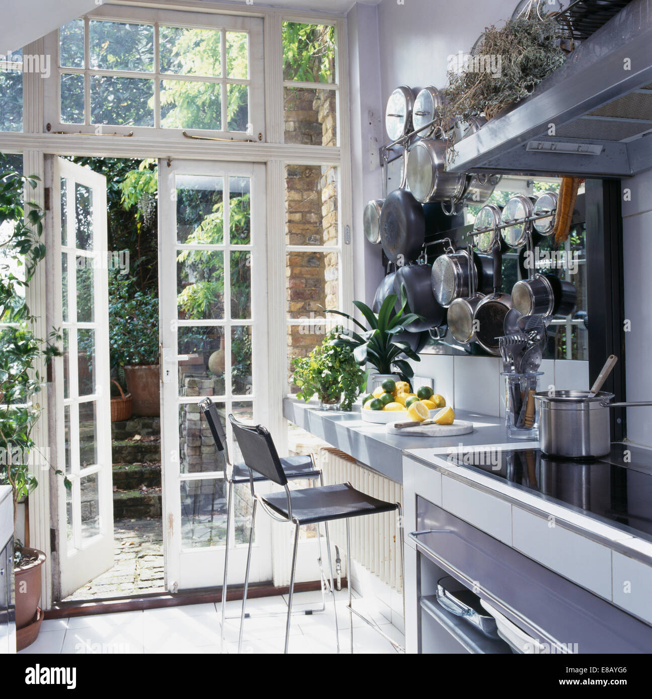 Pale grey kitchen with stools at breakfast bar beside French windows open to small courtyard