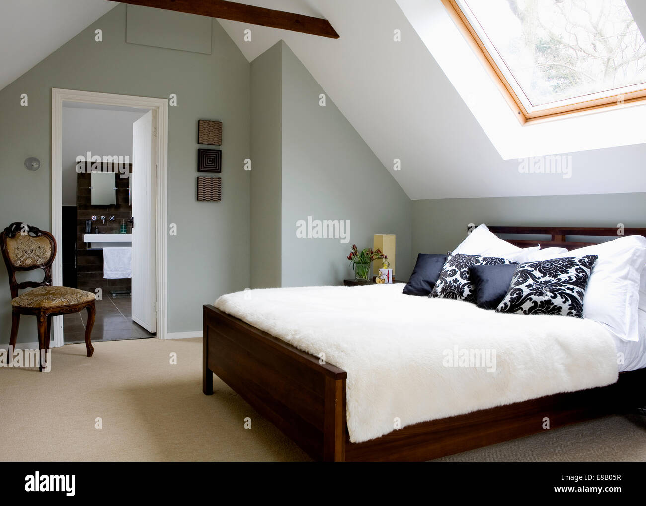 Cream carpet and bed cover in modern attic bedroom with antique chair beside open door to en-suite bathroom Stock Photo