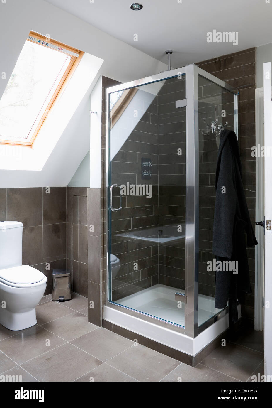 Limestone floor and wall tiles in modern loft conversion shower room with Velux window and glass shower cabinet Stock Photo