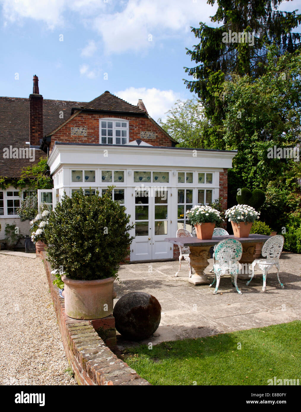 Clipped box in large pot on paved patio with table and chairs in front of country house with conservatory extension Stock Photo