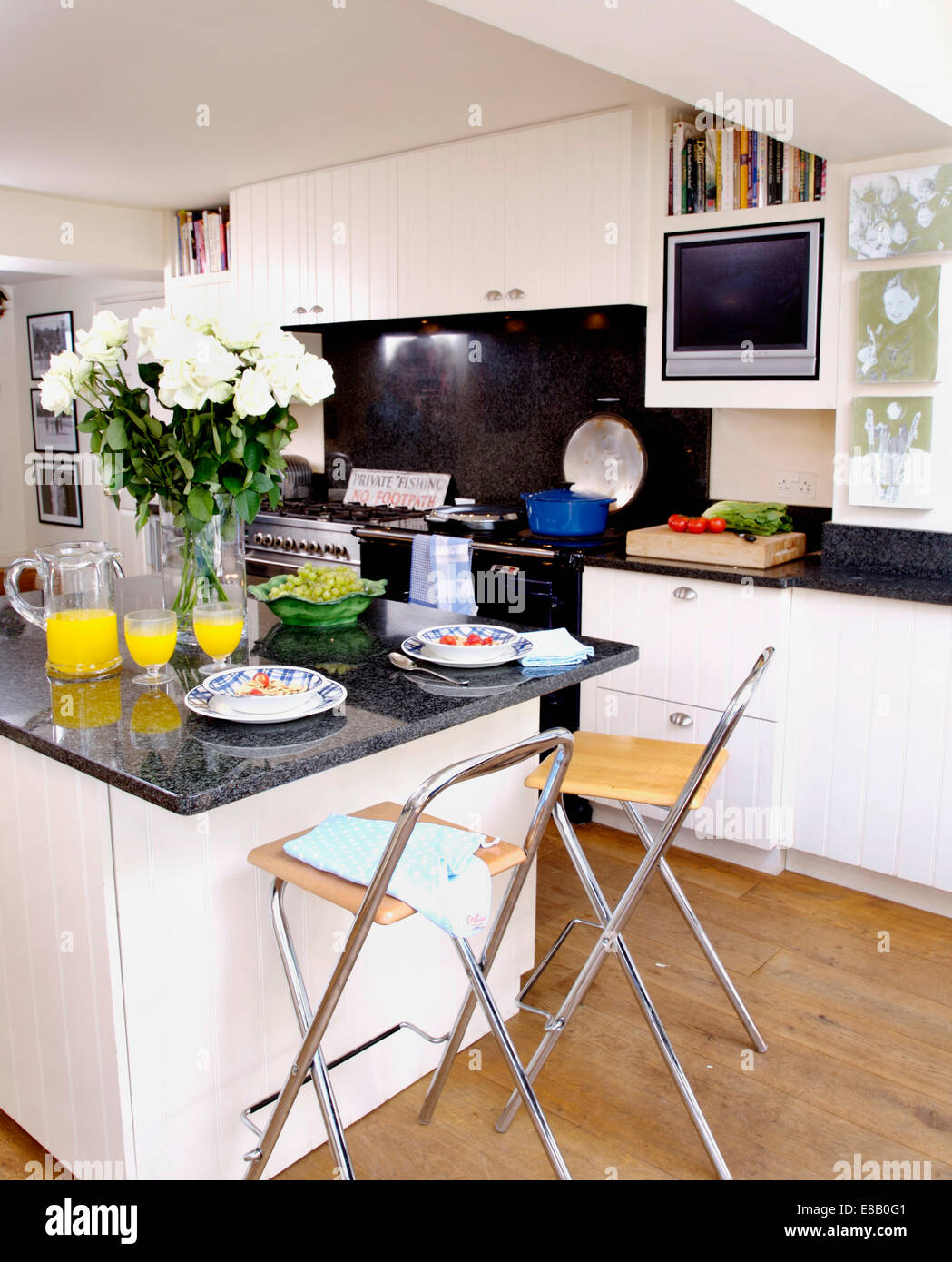 Stools at breakfast bar with vase of white roses and jug of orange juice on granite worktop in