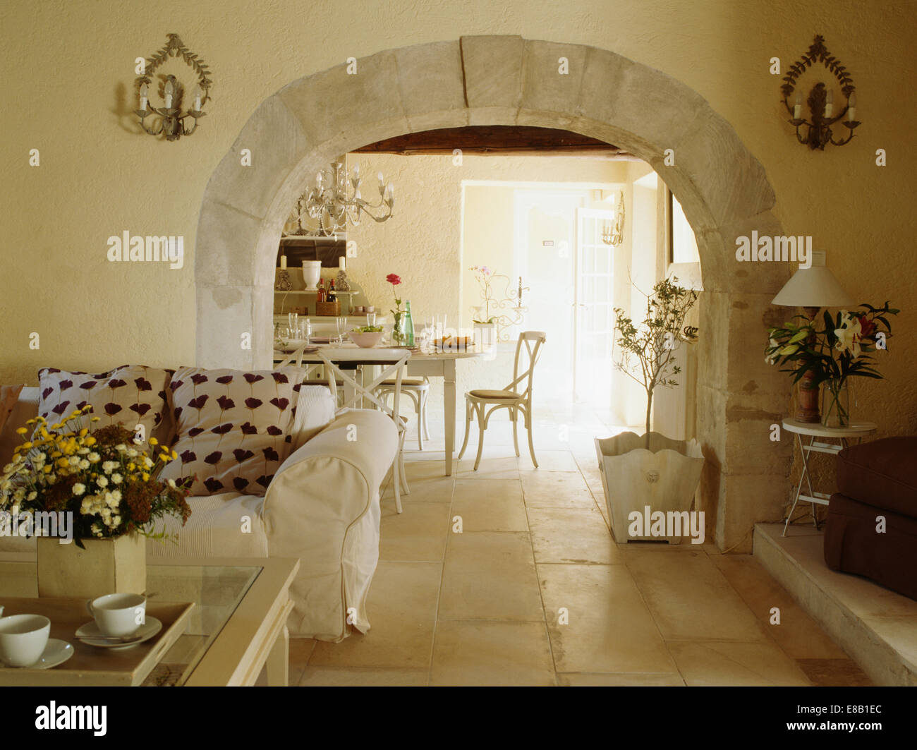 Stone flooring in French country living room with white sofa beside stone-edged arch to dining room Stock Photo