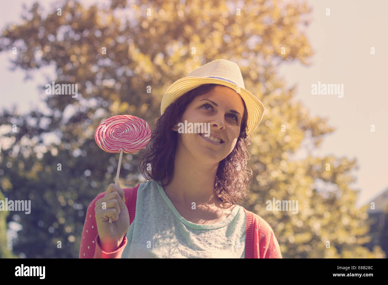 Cute hipster teenage girl smiling and holding a big lollipop. Outdoor shot, retro colors Stock Photo