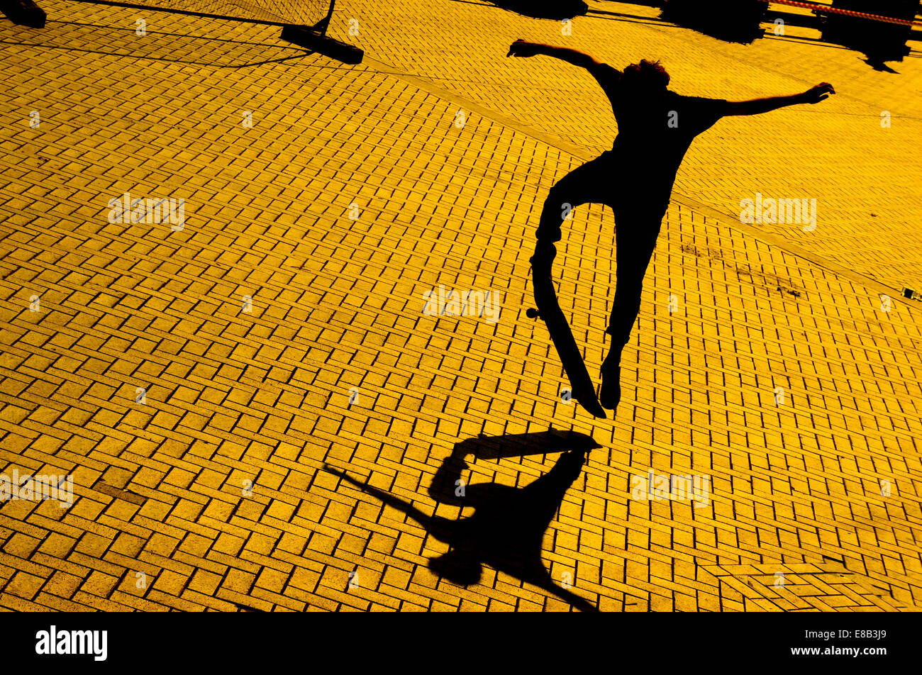 A skateboarder at dusk makes a jump casting a shadow on the brick paved surface. Stock Photo