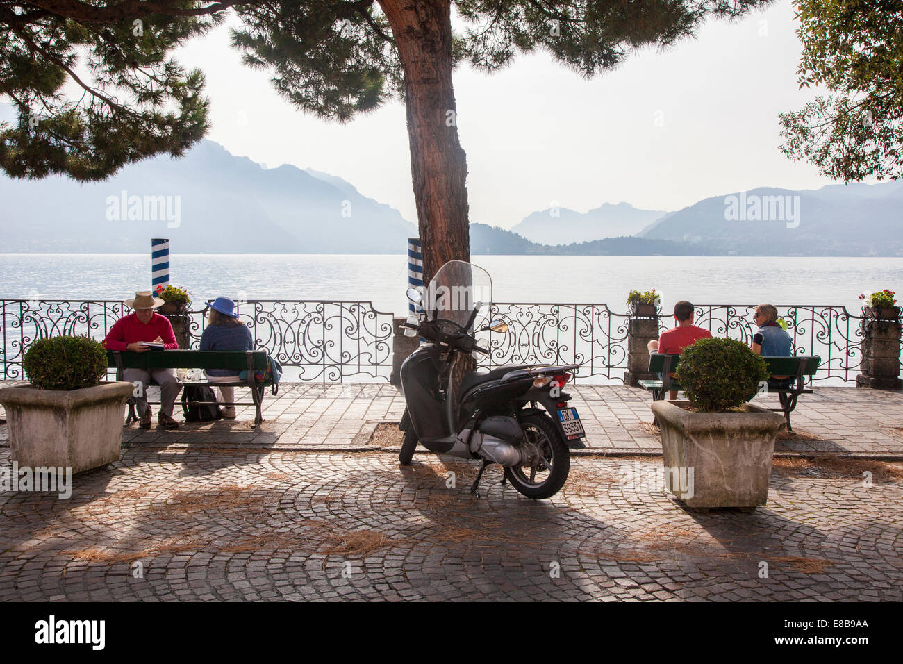 Couple sitting on the lake front promenade enjoying the sunshine and views of lake Como, Menaggio, Lake Como, Lombardy, Italy Stock Photo
