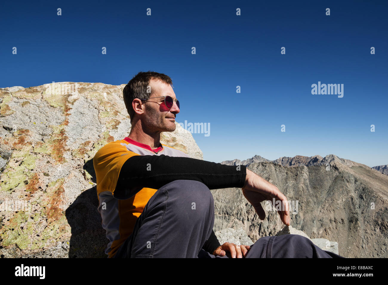 middle aged man sitting on a mountain top leaning against a rock Stock Photo