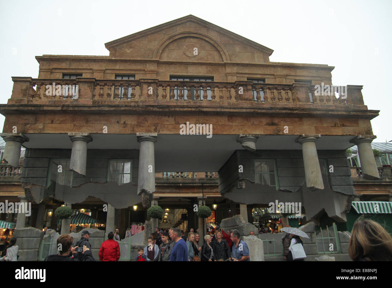 London, UK 4th October 2014.  Londoners seen admiring the levitating artwork at the Covent Garden piazza. The facade of the Market Building in the piazza at Covent Garden, London has been replicated as a drifting artwork by British artist Alex Chinneck. Photo by David Mbiyu/ Alamy Live News Stock Photo