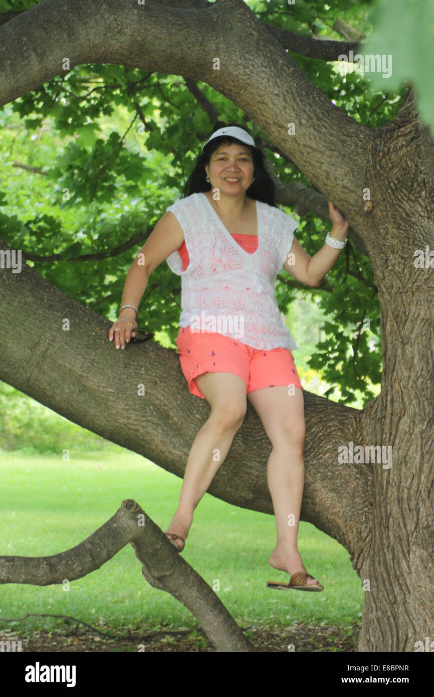 Mature Asian Woman Wearing Shorts Sitting On A Large Branch Of A Big