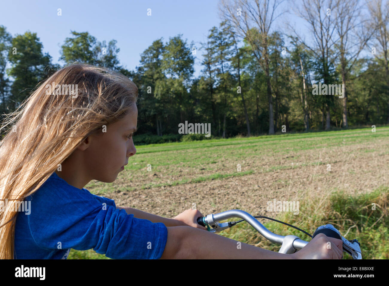A young girl, looking serious and determined, rides a bicycle through the open countryside. Model Released. Stock Photo