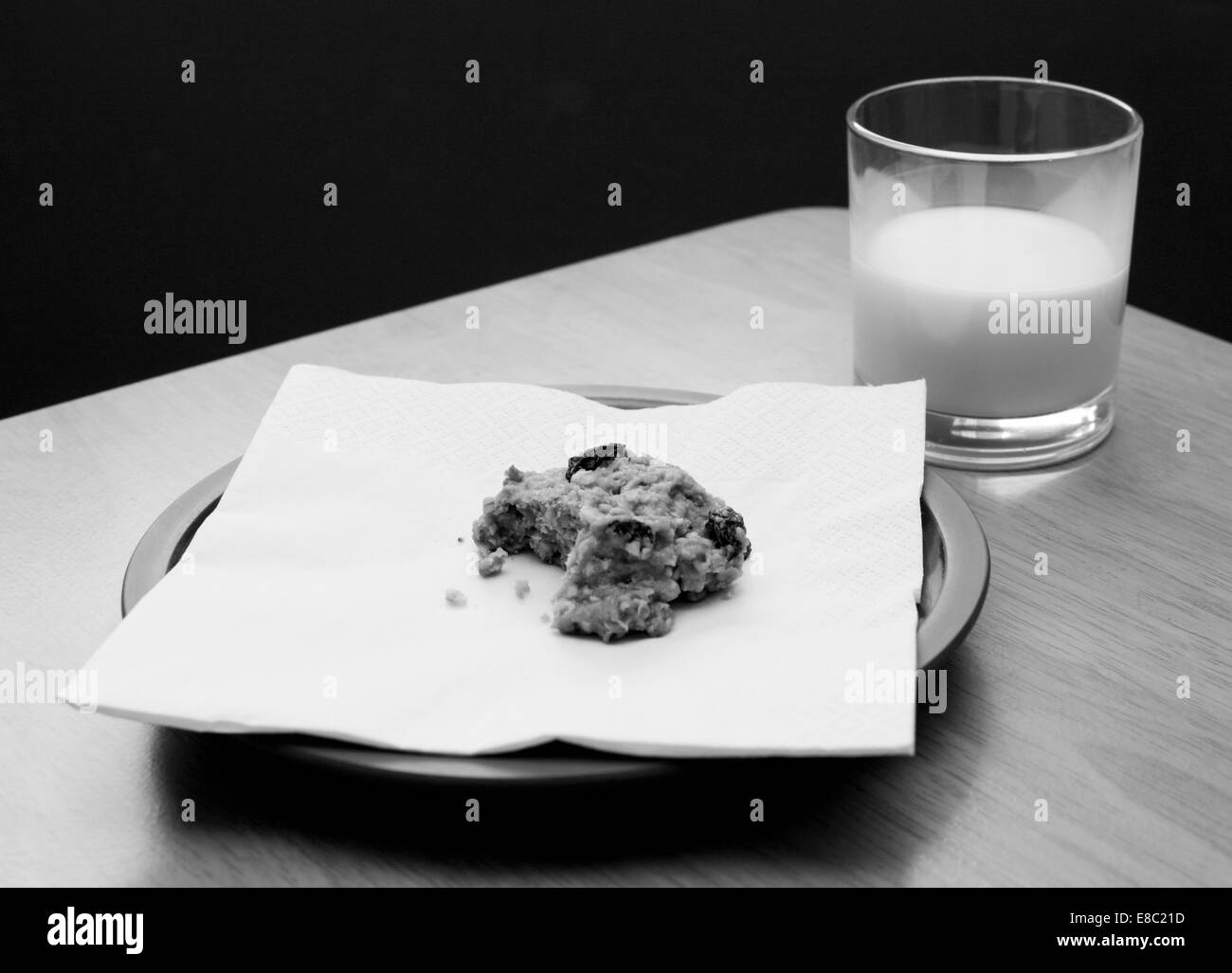 Half-eaten oatmeal raisin cookie with a half drunk glass of milk - monochrome processing Stock Photo