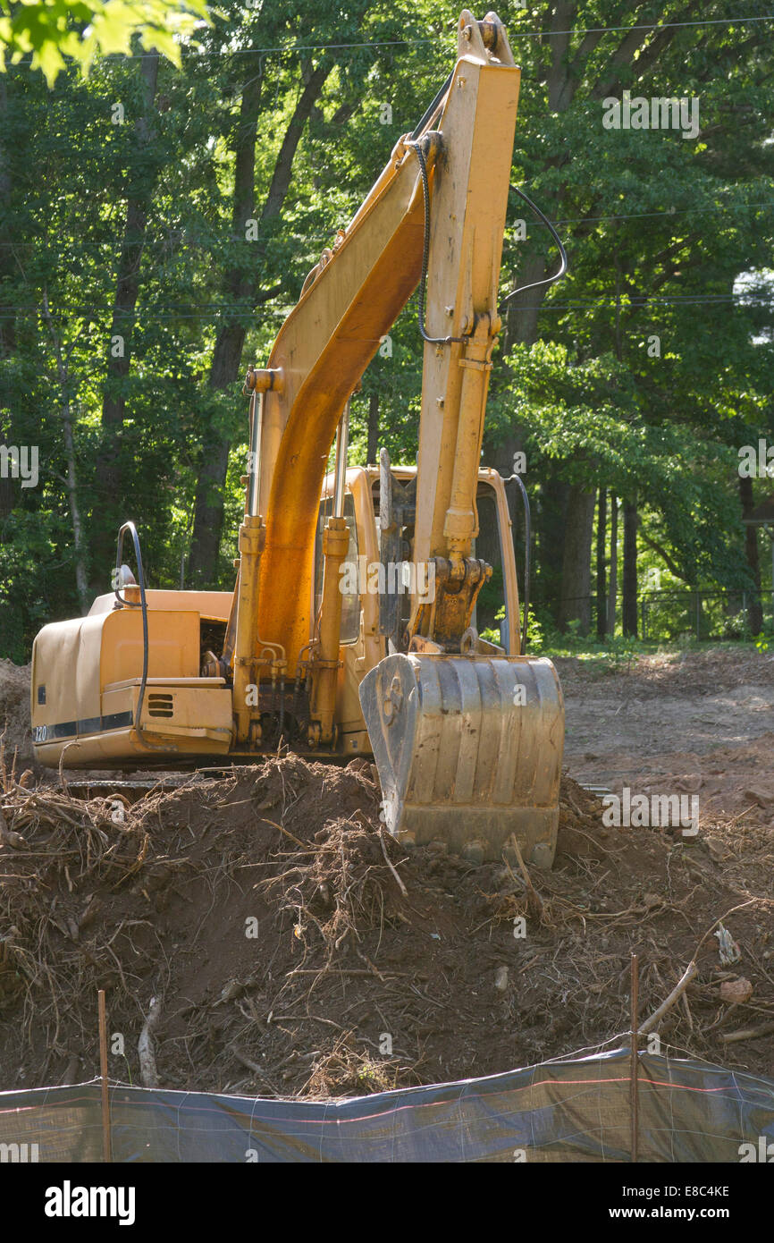 A bright yellow earthmover truck with a big shovel dug halfway into a pile of dirt, sits abandoned and idle Stock Photo