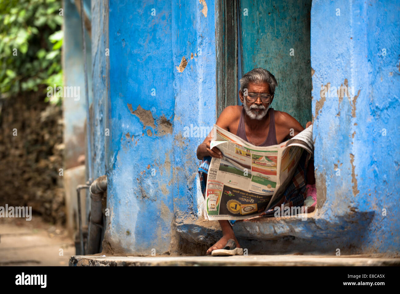 Indian man sitting on his doorstep reading a local newspaper Stock Photo