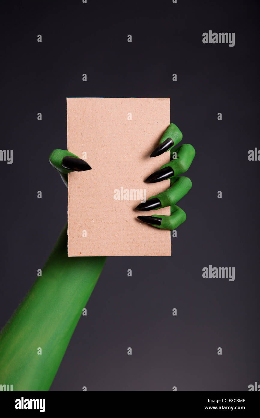 Green monster hand with black nails holding blank piece of cardboard, Halloween theme Stock Photo
