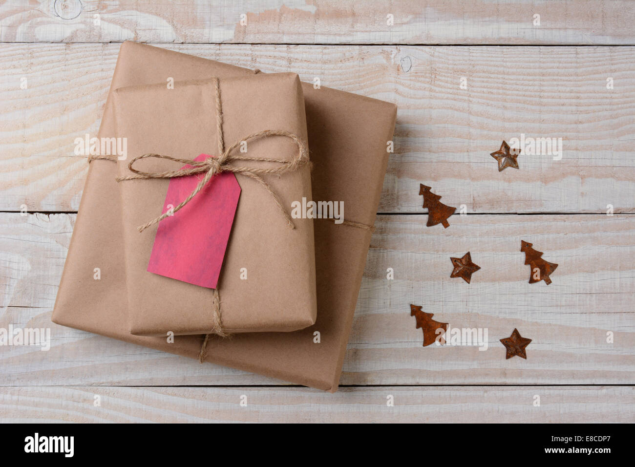 A high angle view of plain brown paper wrapped presents with red tags on a white rustic table. Small rusty metal ornaments in st Stock Photo