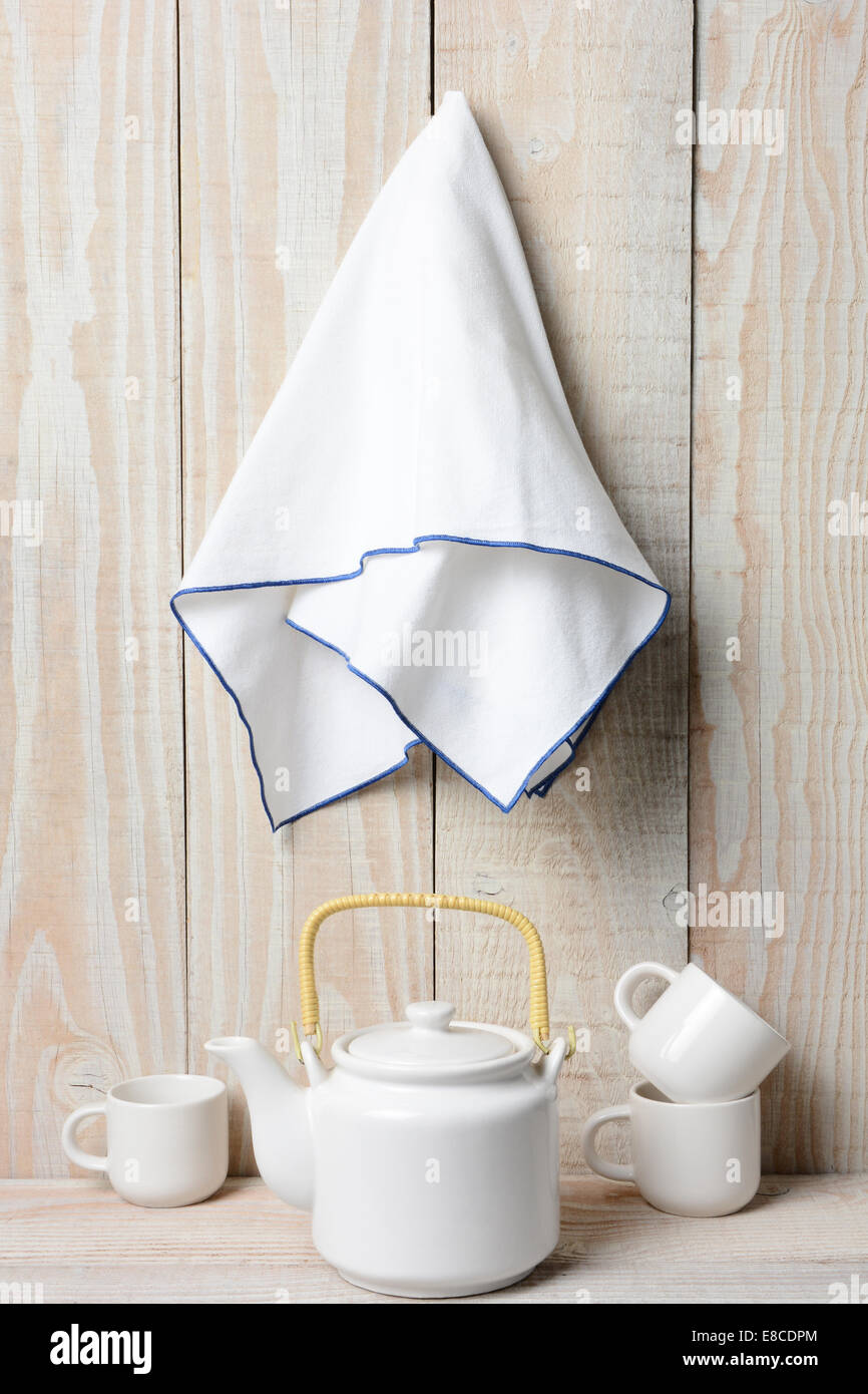 A white tea set on a rustic whitewashed setting with a towel hanging on the wall. Stock Photo