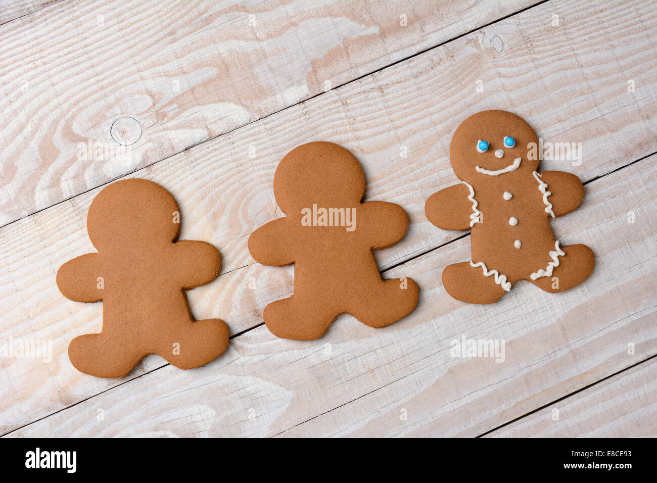 HIgh angle view of three gingerbread men on a rustic white kitchen table. Two cookies are  plain and without icing while one is Stock Photo