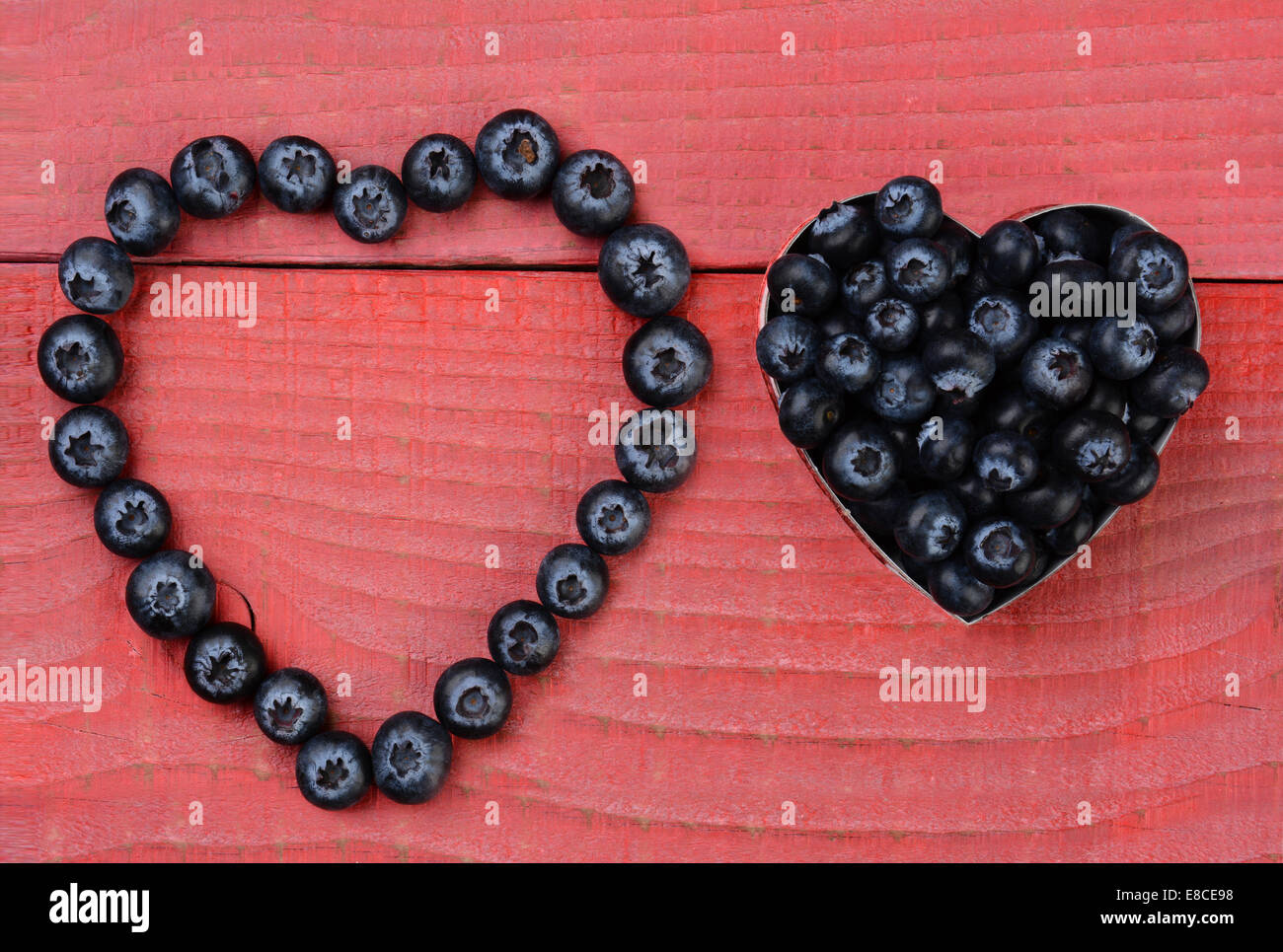 Two different heart shapes made from blueberries on a red wood ...