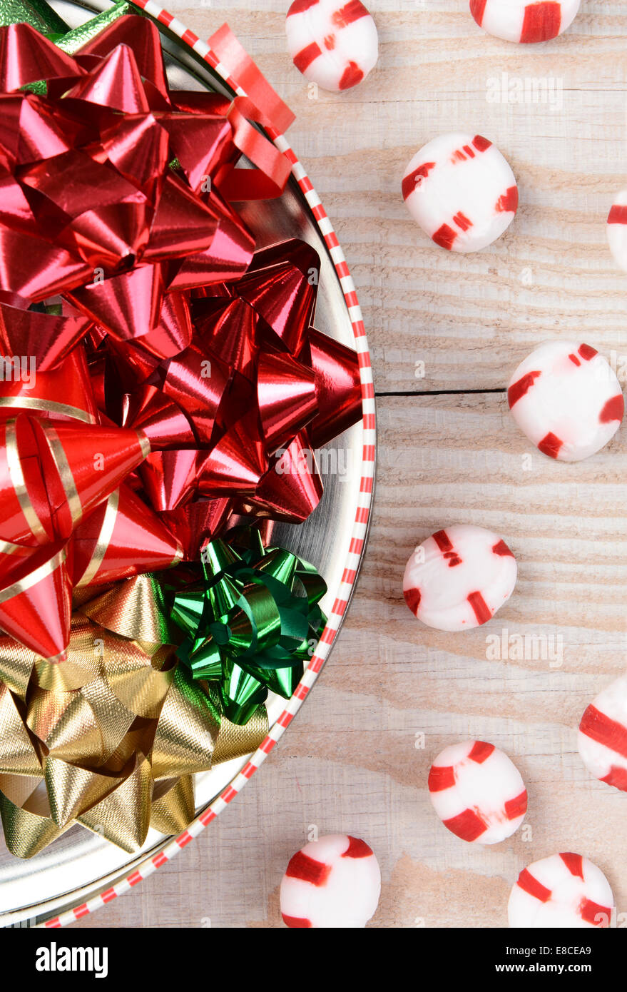 High angle closeup shot of a round tin full of Christmas ribbons on a white wood table with red and white mints scattered. Stock Photo