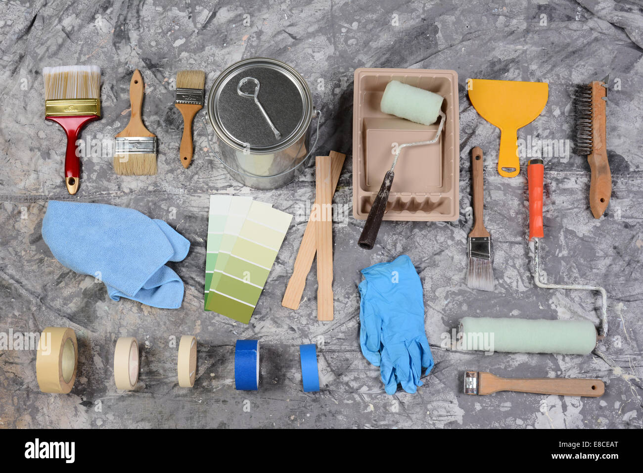 High angle shot of the tools needed to paint spread out on a drop cloth. Items include, paint can, brushes, rollers, tray, tape, Stock Photo