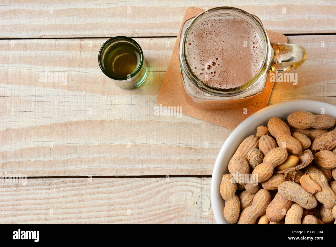 High angle shot of a glass of beer, a whiskey shot and a bowl of peanuts on a white wood table. Horizontal format with copy spac Stock Photo