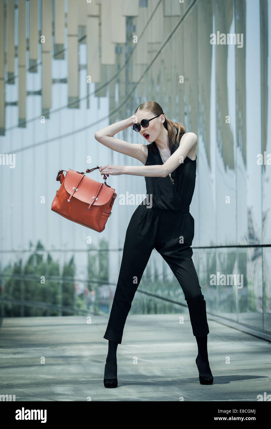 Beautiful young Asian business woman with leather bag around a glass office building Stock Photo