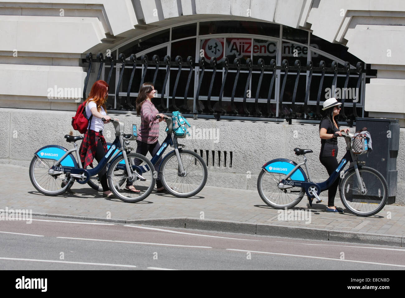 Three females walking with their cycles along a London street Stock Photo