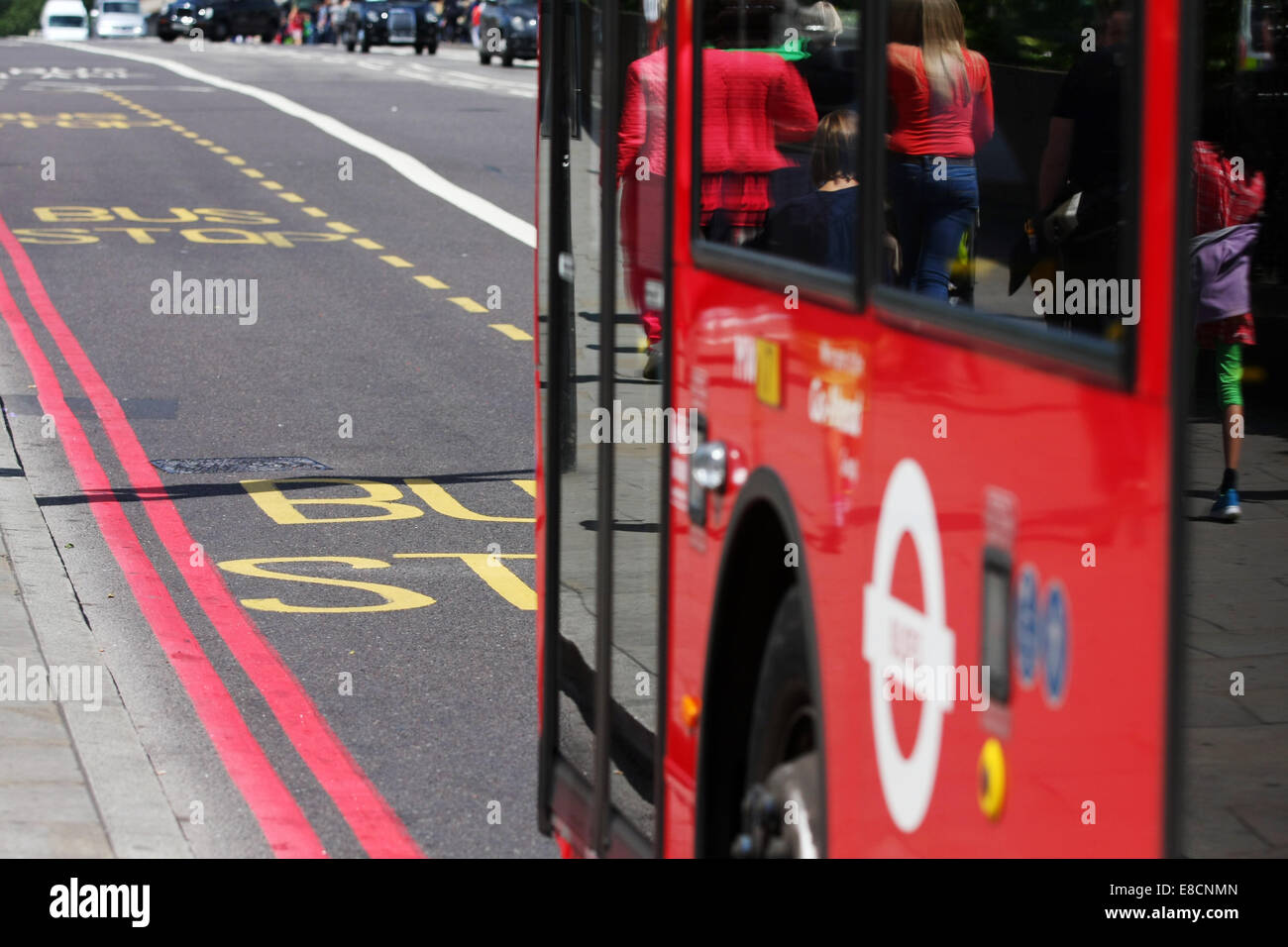 A red London bus traveling in a bus lane and approaching a bus stop in London Stock Photo